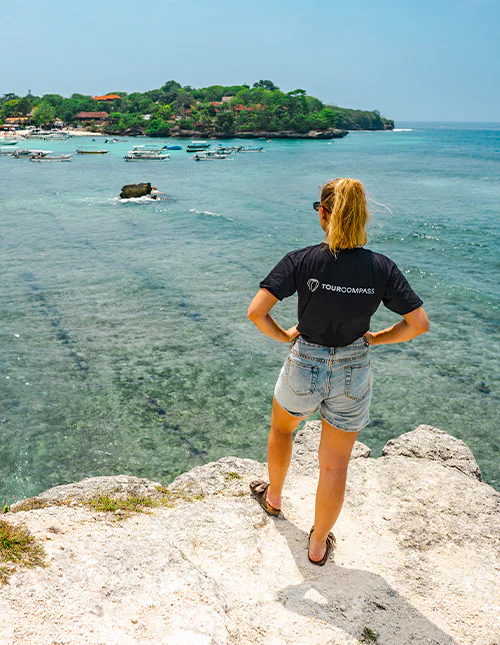 Eine Frau im TourCompass-T-Shirt genießt die Aussicht auf das türkisfarbene Wasser