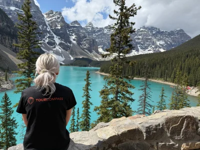 Eine Frau im TourCompass-T-Shirt blickt vom Ufer des Lake Louise in Kanada über das Wasser.