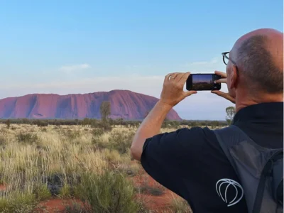Ein Mann fotografiert den Uluru in Australien mit seinem Handy.