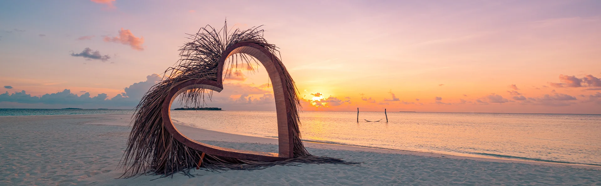 Herzskulptur an einem tropischen Strand bei Sonnenuntergang